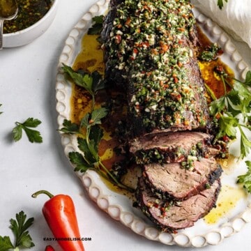 a platter with partially sliced reverse seared beef tenderloin. topped with chimichurri sauce