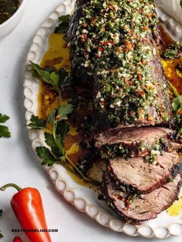 a platter with partially sliced reverse seared beef tenderloin. topped with chimichurri sauce