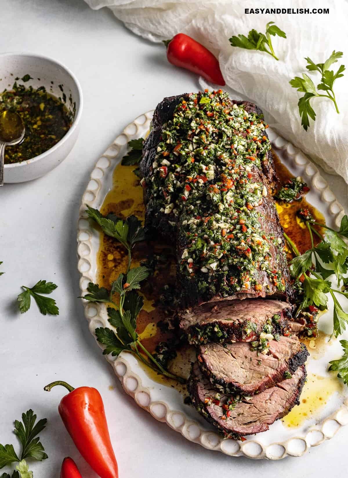 a platter of cooked roast topped with chimichurri sauce and some red chilli.