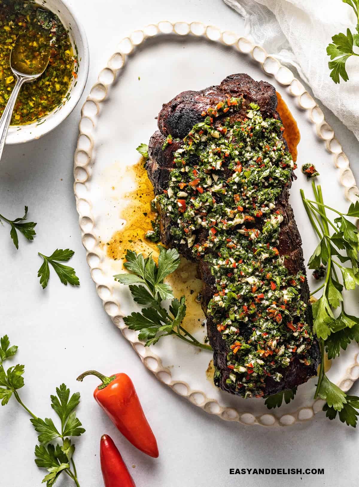 whole smoked beef tenderloin with Argentinian chimichurri sauce and some garnishes on the side.