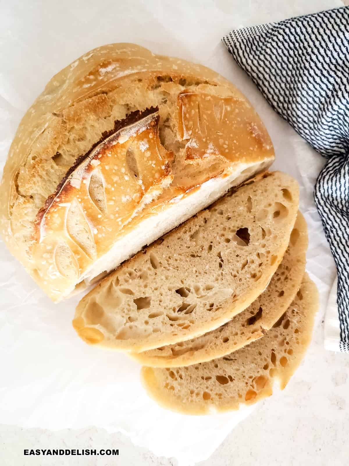 basic sourdough bread part whole and part sliced over parchment paper.