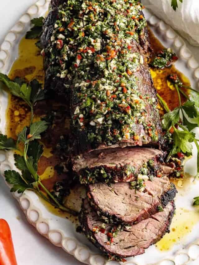 A platter with partially sliced reverse seared beef tenderloin. topped with chimichurri sauce