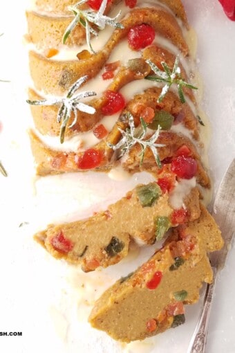 gluten-free fruit cake decorated for Christmas and partially sliced over parchment paper.