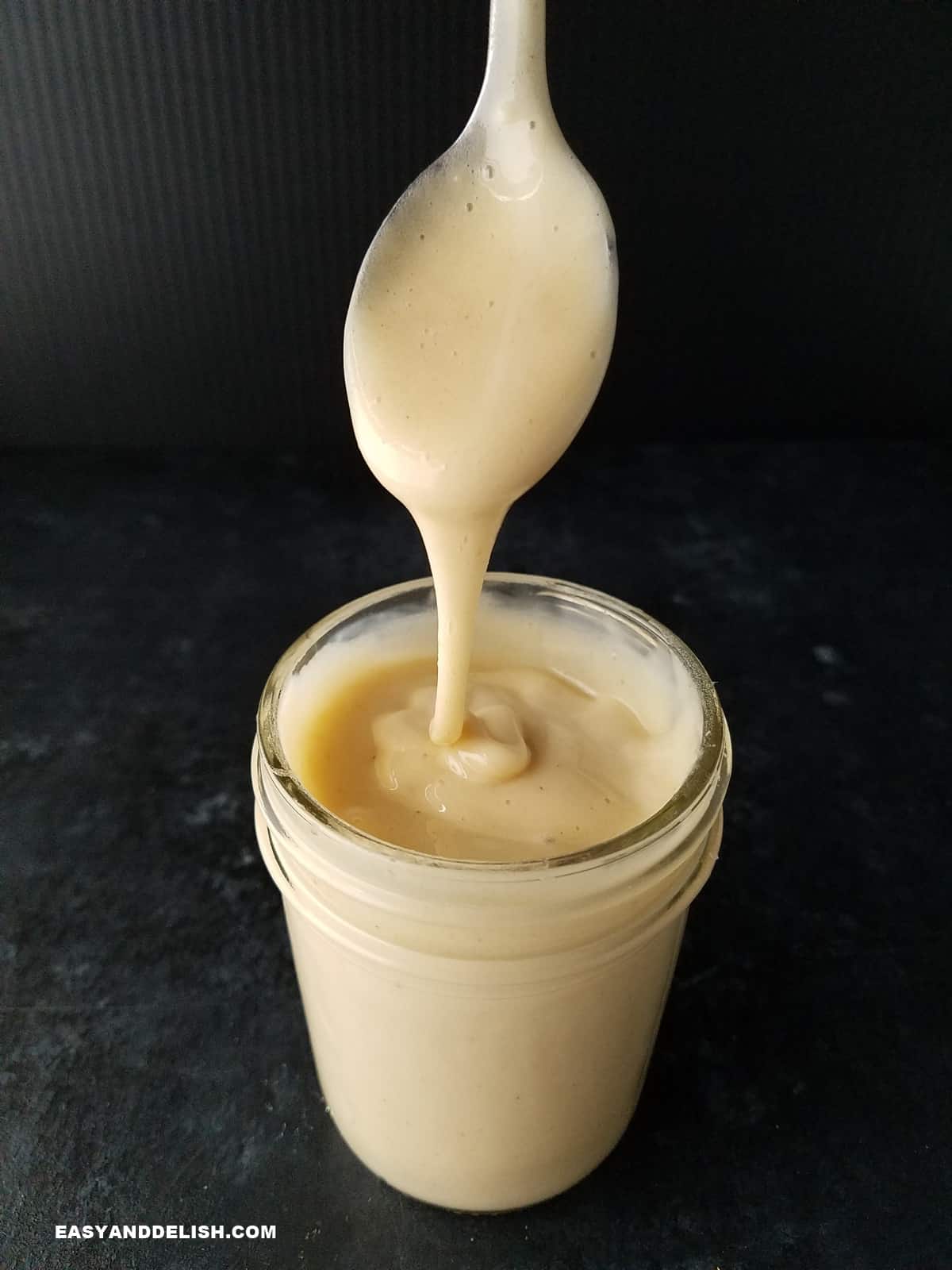 a jar of sugar-free condensed milk with a spoon held over dripping into it.