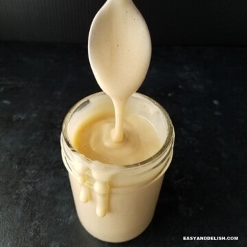 close up of a jar of sugar-free keto condensed milk dripping on the sides with a spoon held on top.