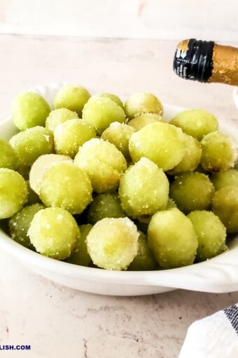 a bowl full of suagred prosecco grapes with a bottle of that sparkling wine nearby.