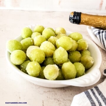 a bowl full of suagred prosecco grapes with a bottle of that sparkling wine nearby.