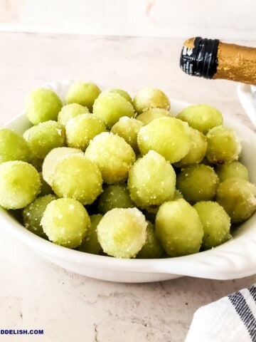 a bowl full of suagred prosecco grapes with a bottle of that sparkling wine nearby.