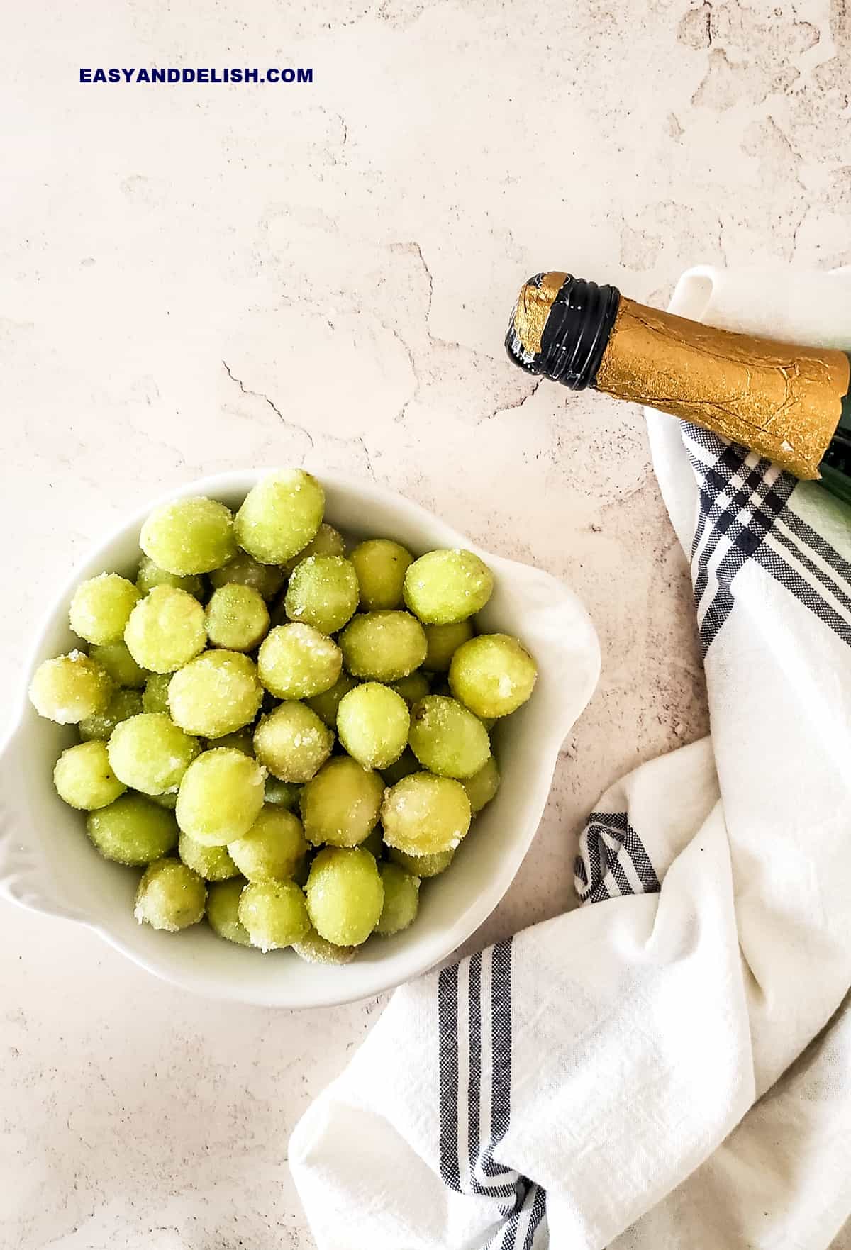 a bowl of fruit coated in sugar with a bottle of wine nearby and a napkin under.