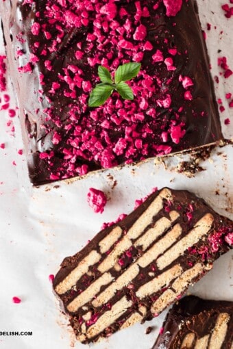 close up of half chocolate biscuit cake sliced garnished with berries and mint leaves.