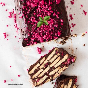 close up of half chocolate biscuit cake sliced garnished with berries and mint leaves.