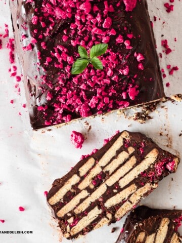 close up of half chocolate biscuit cake sliced garnished with berries and mint leaves.