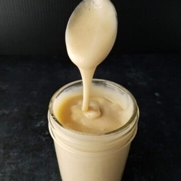 a jar of sugar-free condensed milk with a spoon held over dripping into it.