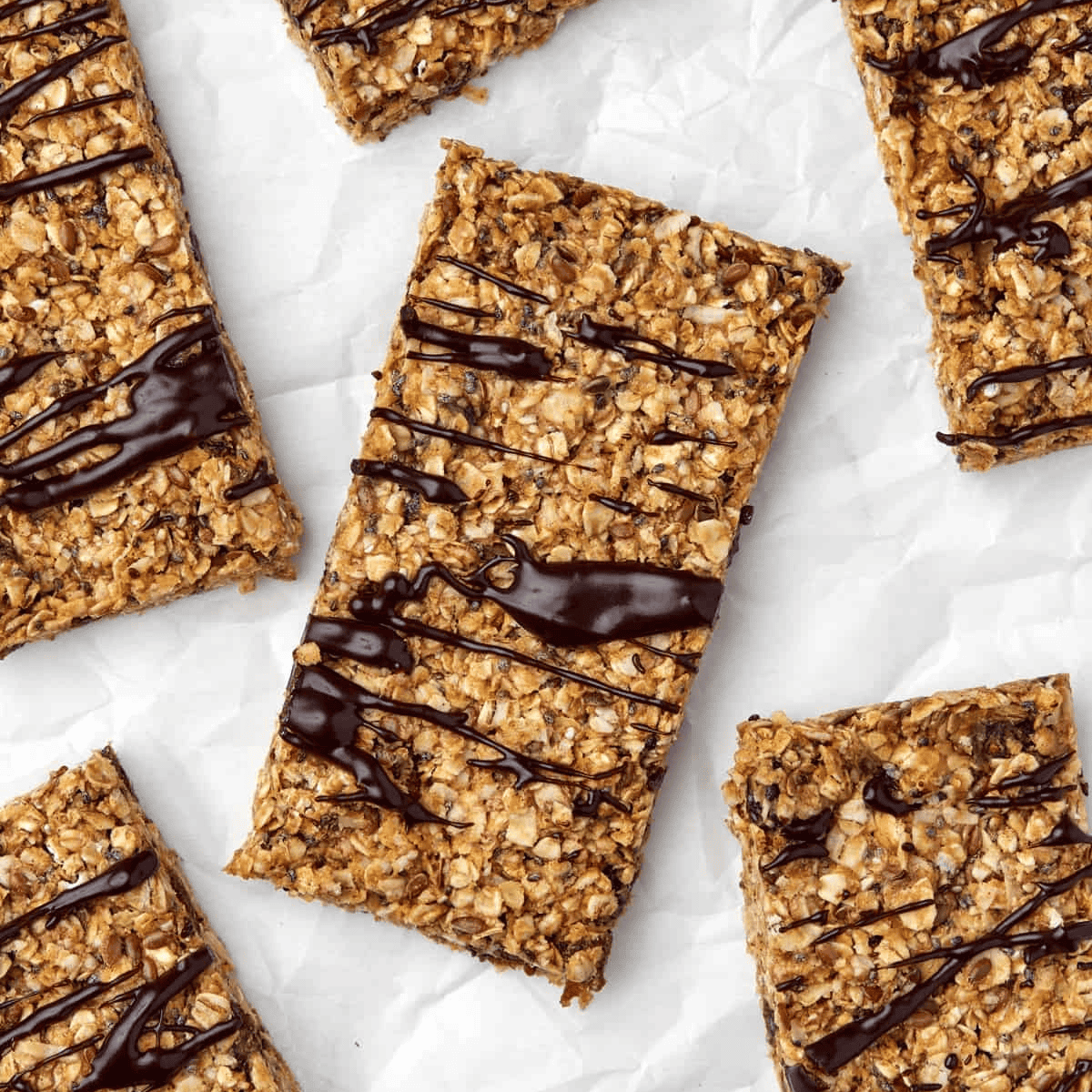 Homemade energy bars drizzled with chocolate on parchment paper.