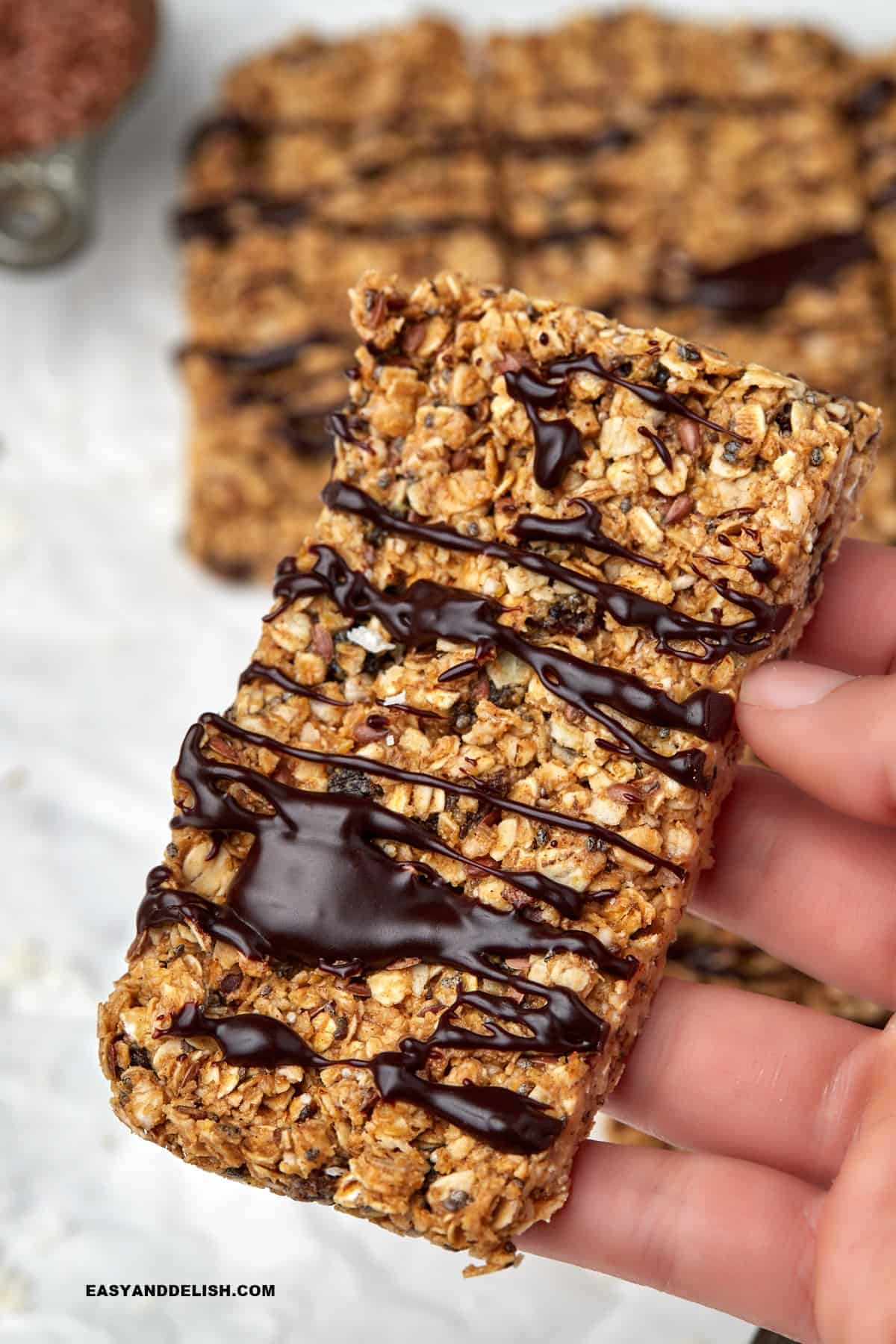 Hand holding a thick oat bar topped with chocolate.