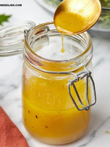 A spoon over a jar with apple cider vinaigrette .