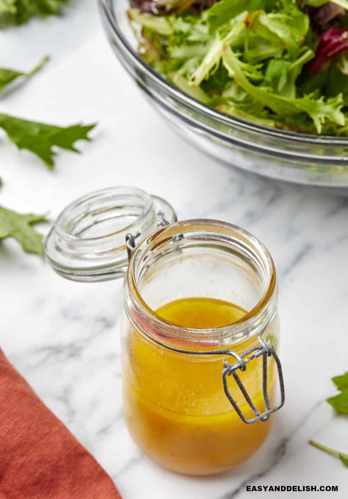 salad dressing with apple cider vinegar in a jar neat a bowl of greens.