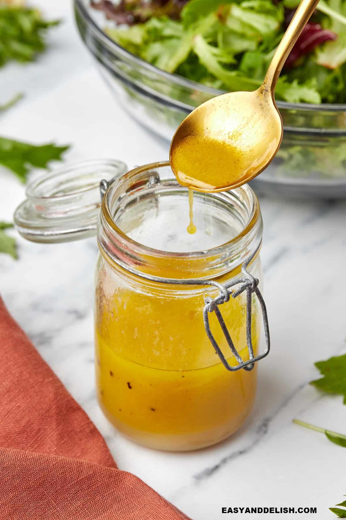 apple cider vinaigrette dressing in a jar with a spoon over it.