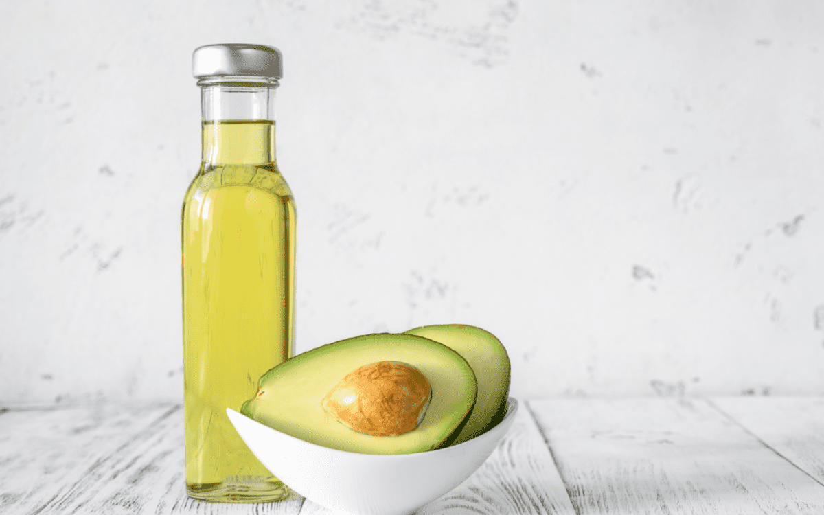 a bottle of olive oil and a two avocado halves in a bowl.
