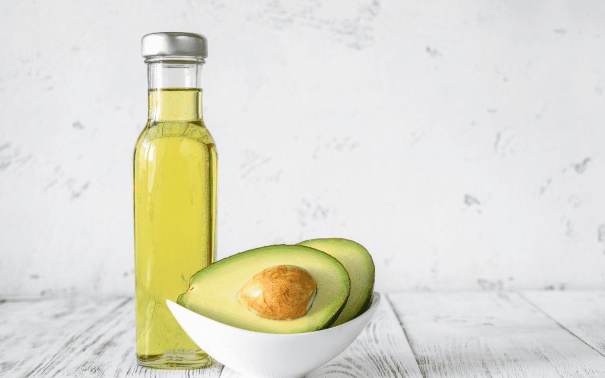 a bottle of olive oil and a two avocado halves in a bowl.