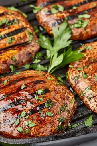 several pieces of grilled mushroom steak topped with sauce and herbs.