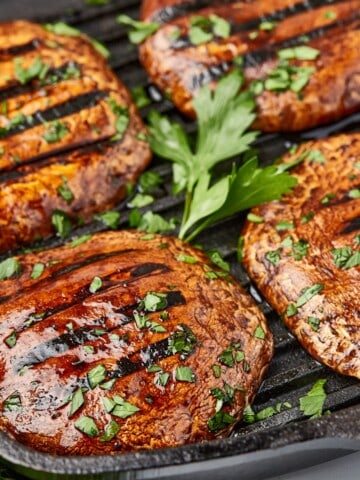 several pieces of grilled mushroom steak topped with sauce and herbs.