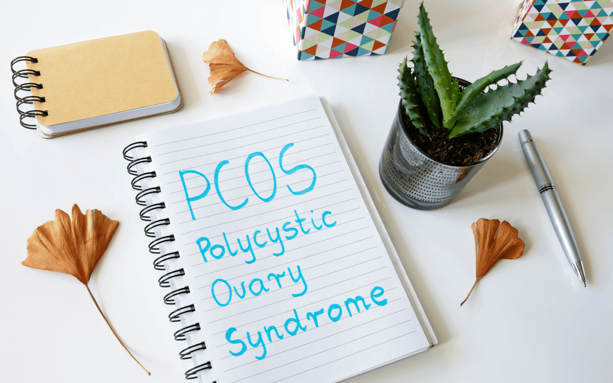 a notebook written PCOS (polycistic ovary syndrome) surrounded by office objects.  