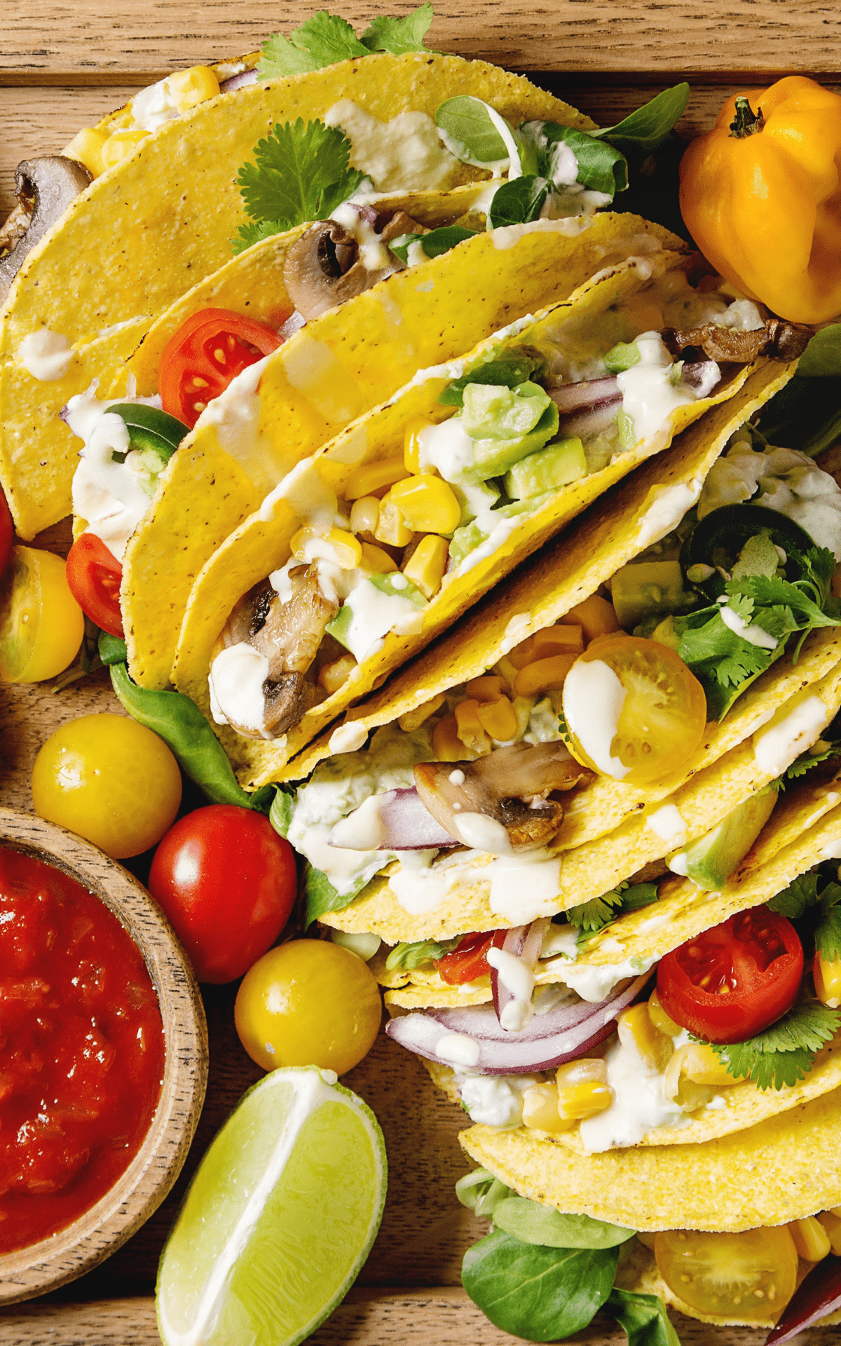 close up of tacos filled with veggie toppings and a bowl of salsa on the side with more vegetables..