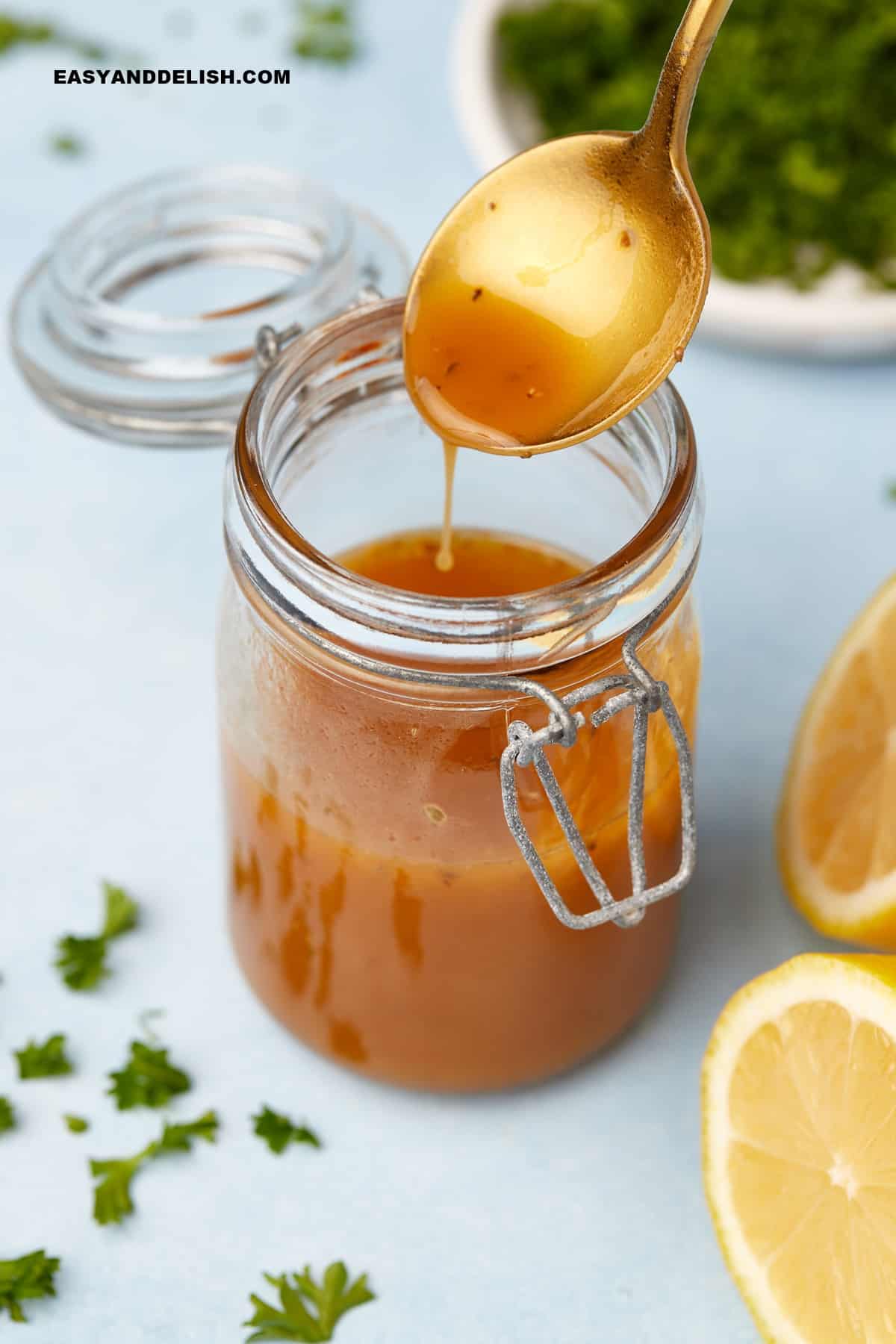 a spoon drizzling some of the mediterranean salad dressing ina  jar.