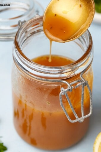 close up iof a jar of mediterranean salad dressing with some in a spoon held over the jar.