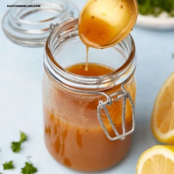 close up iof a jar of mediterranean salad dressing with some in a spoon held over the jar.