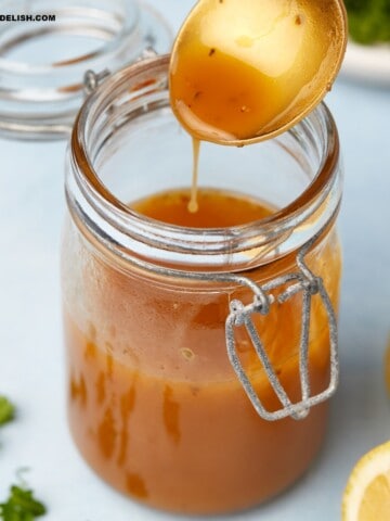 close up iof a jar of mediterranean salad dressing with some in a spoon held over the jar.