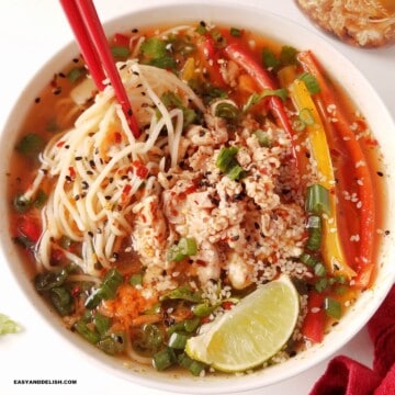 a bowl of gluten-free chicken noodle soup with fresh garnishes on top.