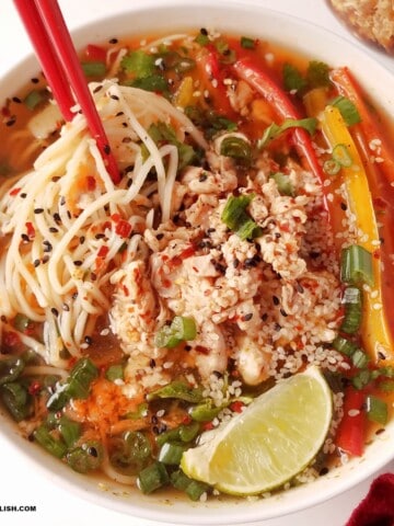 a bowl of gluten-free chicken noodle soup with fresh garnishes on top.