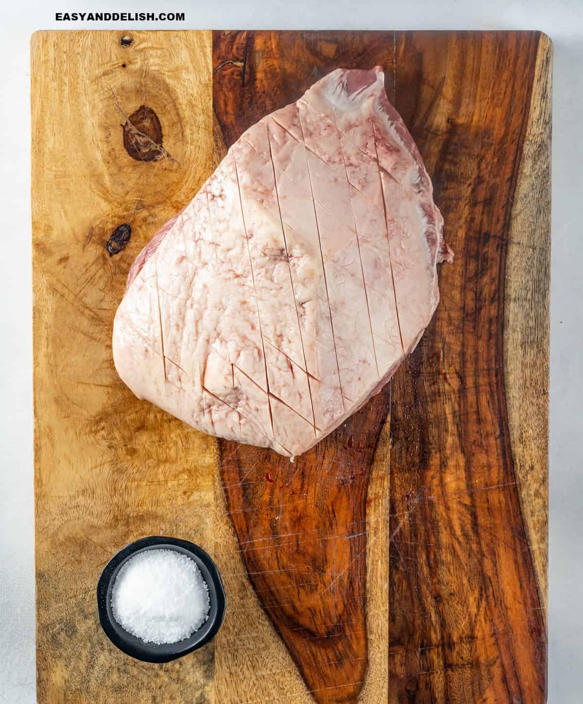 a large piece of fat scored meat on a cutting board with salt on the side.