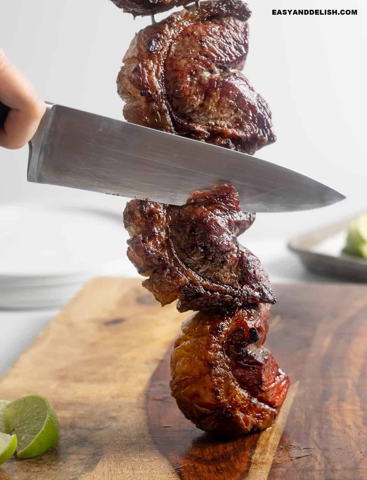 a knife cutting grilled picanha steaks in a skewer.