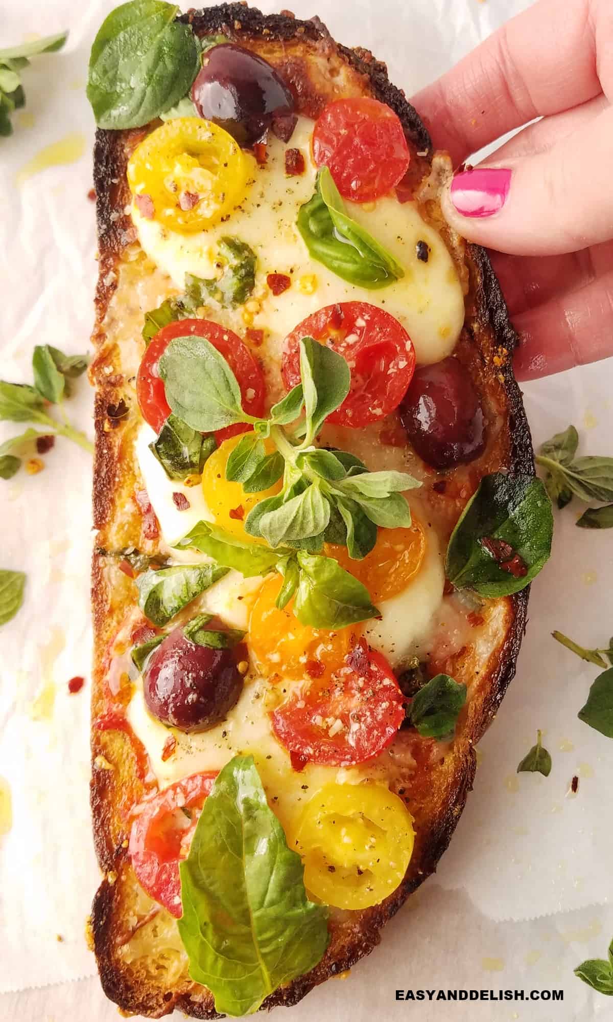 A hand holding a Mediterranean pizza toast .