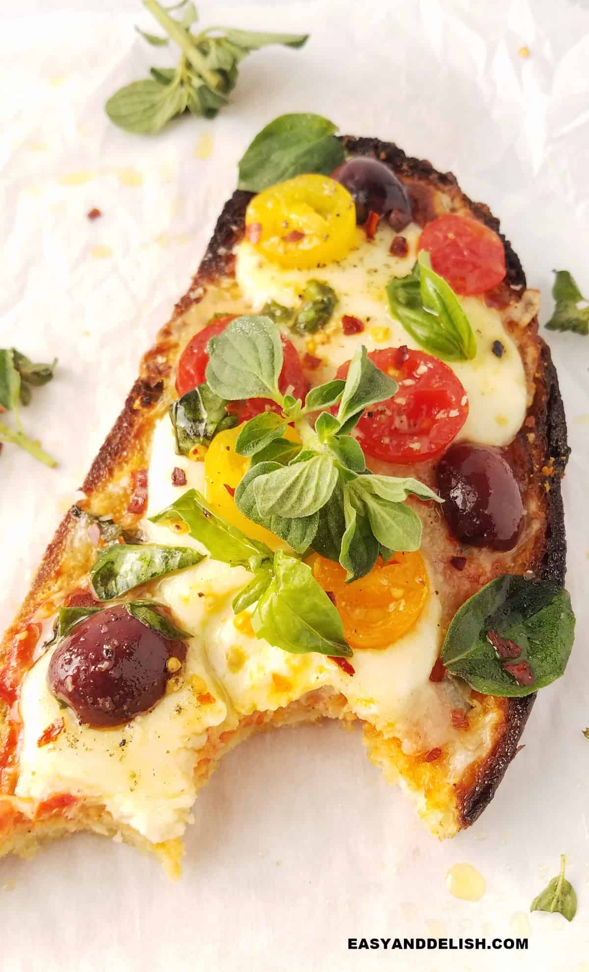 a bitten pizza toast with fresh basil leaves on the side.