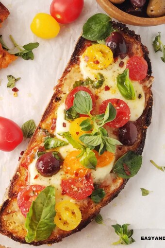 Mediterranean pizza toast on a table with some ingredients around it.