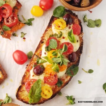 Mediterranean pizza toast on a table with some ingredients around it.