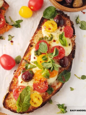 Mediterranean pizza toast on a table with some ingredients around it.