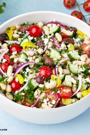 a full bowl of white bean salad with a few ingredients around it.