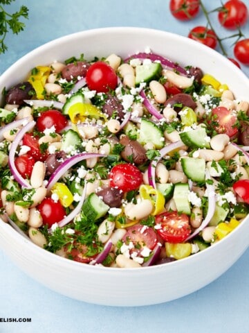 a full bowl of white bean salad with a few ingredients around it.