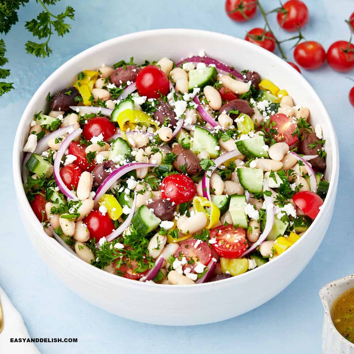 a full bowl of white bean salad with a few ingredients around it.