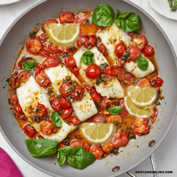 Italian baccala in a skillet topped with a white wine tomato sauce, basil, and lemon.