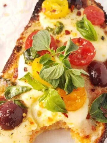 Pizza toast with melted mozzarella, cherry tomatoes, olives and fresh herbs.