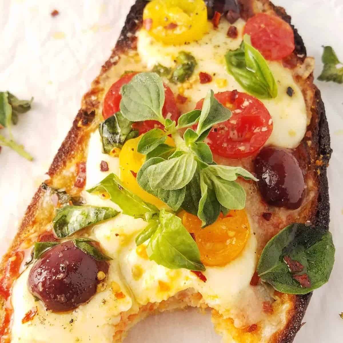 Pizza toast with melted mozzarella, cherry tomatoes, olives and fresh herbs.
