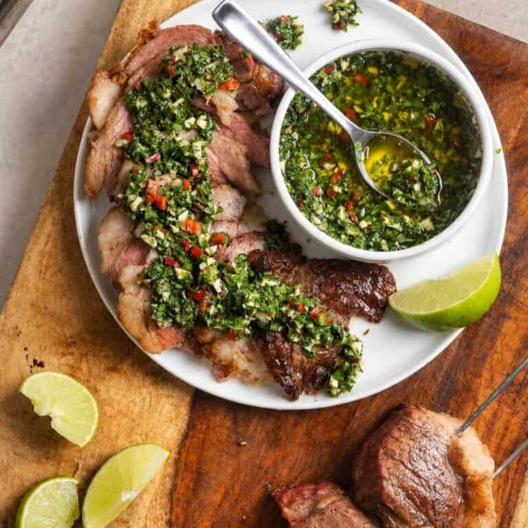 Sliced grilled picanha steak with chimichurri sauce and lime wedges.