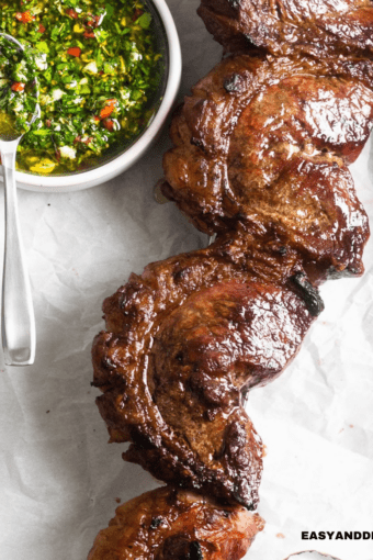 close up of grilled picanha steak in a skewer with a side of chimichurri sauce on a table.