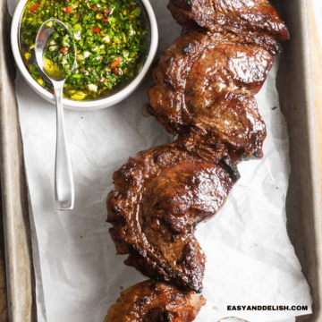 close up of grilled picanha steak in a skewer with a side of chimichurri sauce on a table.